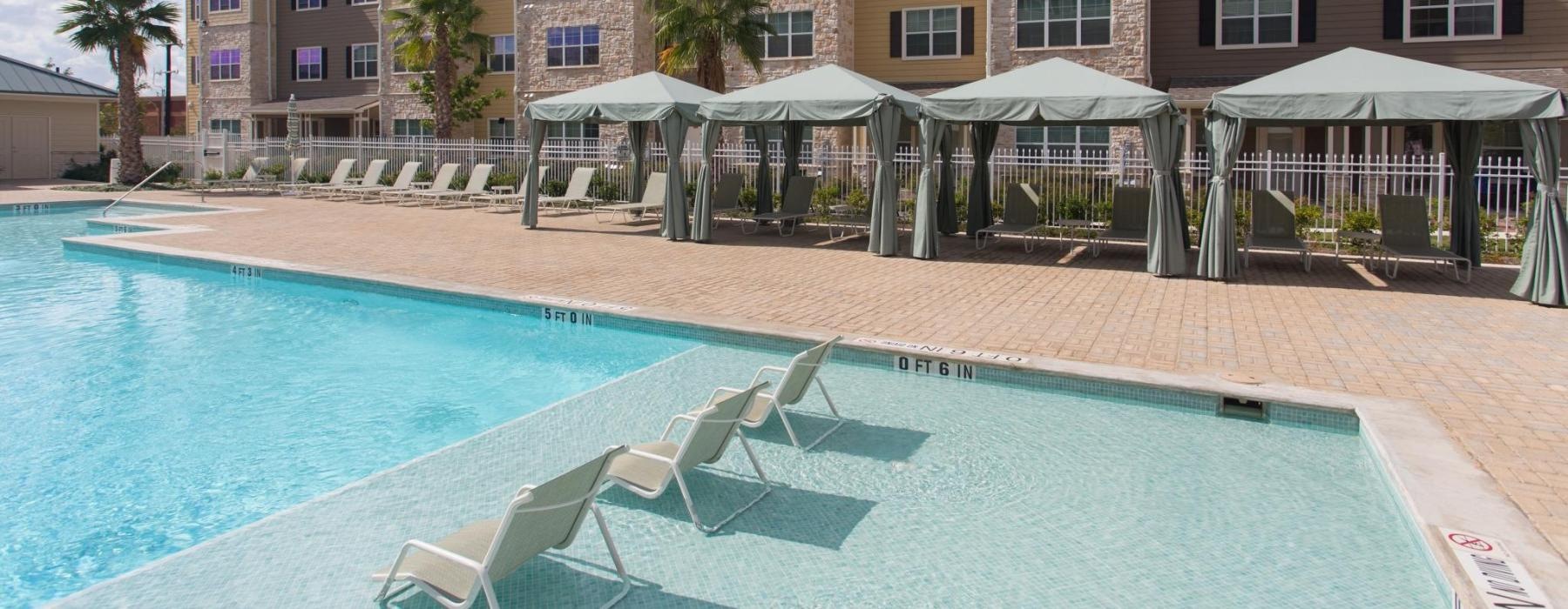 a pool with lounge chairs and umbrellas by a building