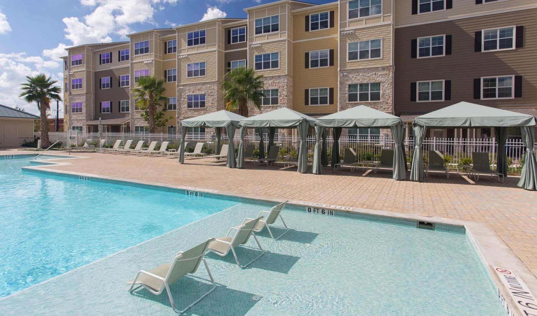 a pool with lounge chairs and umbrellas by a building