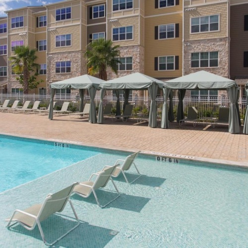 Resort-style swimming pool a pool with lounge chairs and umbrellas by a building