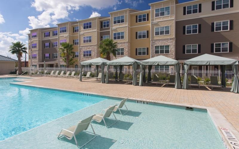 a pool with lounge chairs and umbrellas by a building